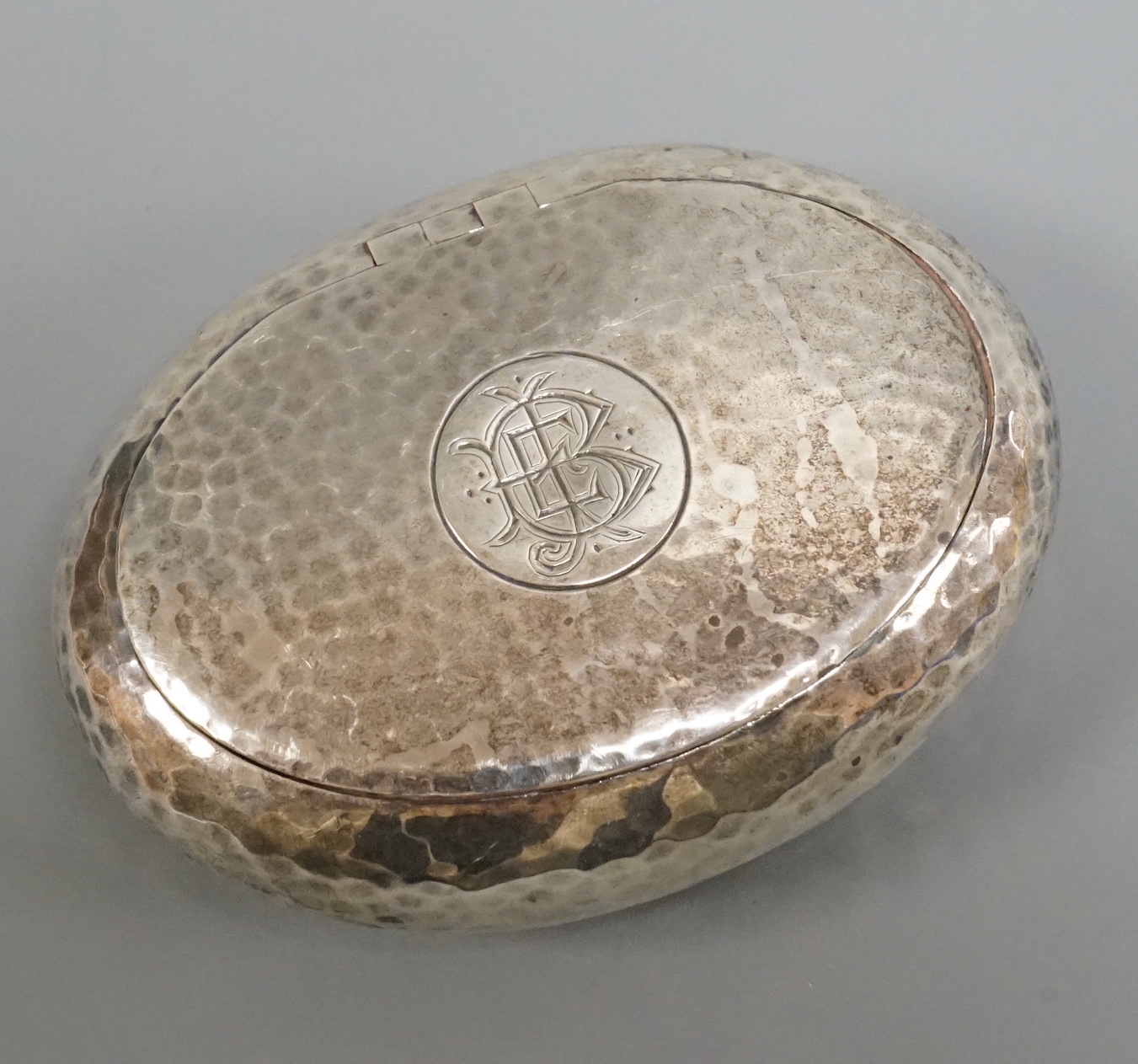 An Edwardian hammered silver oval tobacco box, William M. Hayes, Birmingham, 1908, 86mm.
